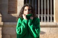 Portrait of beautiful young brunette woman with curly hair and green woollen coat covering her face with the collar of the coat