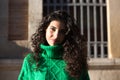 Portrait of a beautiful young brunette woman with curly hair and a green woollen coat. The woman is happy and looks at the camera