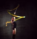 Portrait of beautiful young brunette woman gymnast training calisthenics exercise with yellow ribbon on dark studio background. Royalty Free Stock Photo