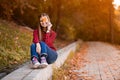 Portrait of beautiful young brunette woman in red shirt and jeans hiding eyes behind autumn leaves