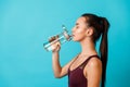 beautiful young brunette woman in sportswear drinks water from a bottle on a blue background, space for text Royalty Free Stock Photo
