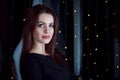 Portrait of beautiful young brunette woman standing in a room with fairy lights on the window Royalty Free Stock Photo