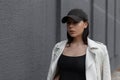 Portrait of a beautiful young brunette woman in a stylish black cap in a vintage white leather jacket in a black t-shirt Royalty Free Stock Photo