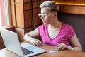 Portrait of beautiful young bussineswoman with short hair in pink t-shirt and eyeglasses is sitting in cafe, trying to order