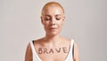 Portrait of a beautiful young caucasian woman with the word Brave painted on her chest, posing with eyes closed isolated