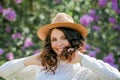 Portrait of beautiful young dark-haired woman with blue eyes in hat near the blooming. Happy model with curly hair. Spring Royalty Free Stock Photo