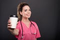 Portrait of beautiful young doctor offering takeaway coffee