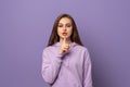Portrait of beautiful young european woman with chestnut hair holding index finger at lips, asking to keep silence or not tell Royalty Free Stock Photo