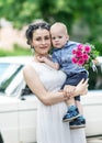 Portrait of a beautiful young female bride holding small baby boy with wedding roses bouquet and looking into camera at sunny summ Royalty Free Stock Photo