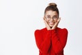 Portrait of beautiful young female entrepreneur in glasses and red sweater, holding hands on cheeks and smiling