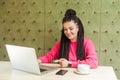 Portrait of beautiful young freelancer with black braided hairstyle in pink blouse is sitting in cafe, trying to order online buy Royalty Free Stock Photo