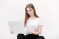 Portrait of a beautiful young girl with blond hair in glasses and a white T-shirt working or studying on a laptop isolated on a Royalty Free Stock Photo