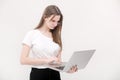 Portrait of a beautiful young girl with blond hair in glasses and a white T-shirt working or studying on a laptop isolated on a Royalty Free Stock Photo