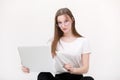 Portrait of a beautiful young girl with blond hair in glasses and a white T-shirt working or studying on a laptop isolated on a Royalty Free Stock Photo