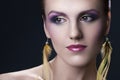 Portrait of beautiful, young girl with bright colorful makeup and feather earrings on black background