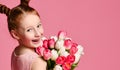 Portrait of a beautiful young girl in dress holding big bouquet of irises and tulips over pink background