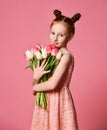 Portrait of a beautiful young girl in dress holding big bouquet of irises and tulips isolated over pink background