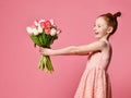 Portrait of a beautiful young girl in dress holding big bouquet of irises and tulips isolated over pink background