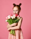 Portrait of a beautiful young girl in dress holding big bouquet of irises and tulips isolated over pink background