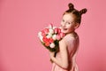 Portrait of a beautiful young girl in dress holding big bouquet of irises and tulips isolated over pink background