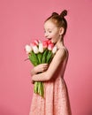 Portrait of a beautiful young girl in dress holding big bouquet of irises and tulips isolated over pink background