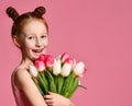 Portrait of a beautiful young girl in dress holding big bouquet of irises and tulips isolated over pink background