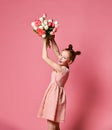 Portrait of a beautiful young girl in dress holding big bouquet of irises and tulips isolated over pink background