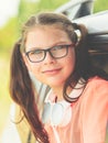 Portrait of a cute young girl in glasses with headphones around her neck - sitting by the open window of the car Royalty Free Stock Photo