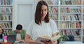 Portrait of beautiful young girl holding book in library bookshelf background looking at the camera. College education Royalty Free Stock Photo