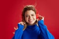 Portrait of beautiful young girl listening to music in headphones, smiling, enjoying against red studio background Royalty Free Stock Photo