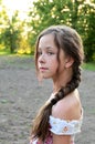 Portrait of beautiful young girl with long hair braided in braid, dressed in summer dress against background of green foliage. Royalty Free Stock Photo