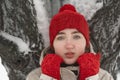 Portrait of beautiful young girl in red knitted hat and mittens warms up near tree in park. Sad girl. Pleasant winter weather Royalty Free Stock Photo