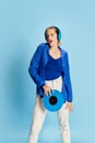 Portrait of beautiful young girl in stylish clothes posing in headphones and vinyl over blue background Royalty Free Stock Photo