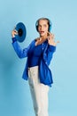 Portrait of beautiful young girl in stylish clothes posing in headphones and vinyl over blue background. Lovely melody Royalty Free Stock Photo