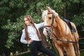 Portrait beautiful young girl in white shirt and black pants with beauty long hair next horse in forest. Fashionable elegance woma