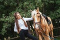 Portrait beautiful young girl in white shirt and black pants with beauty long hair next horse in forest. Fashionable elegance woma Royalty Free Stock Photo