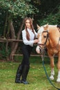 Portrait beautiful young girl in white shirt and black pants with beauty long hair next horse in forest. Fashionable elegance woma Royalty Free Stock Photo