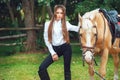 Portrait beautiful young girl in white shirt and black pants with beauty long hair next horse in forest. Fashionable elegance woma Royalty Free Stock Photo