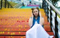 Portrait of a beautiful, young girl who sits on the stairs and listens to music on headphones, in the street, in summer Royalty Free Stock Photo