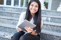 Portrait of a beautiful young Indian girl, business woman, smiling, sitting on the steps, looking into tablet