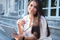 Portrait of a beautiful indian girl. Business woman smiling, holding glasses and tablet in her hands, sitting on the steps of an Royalty Free Stock Photo