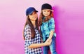 Portrait of beautiful young mother with little girl child wearing checkered shirts, baseball cap in city on pink background Royalty Free Stock Photo