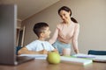 Portrait of beautiful young mother smiling and looking at small teen son with pen at table. Royalty Free Stock Photo