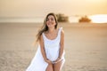 Portrait of beautiful young pregnant woman wearing white dress posing on the beach at sunset. Royalty Free Stock Photo