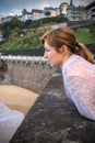 Portrait of beautiful young red haired woman leaning on the wall, observing waves and surfers on the shore of atlantic coast