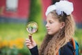 Portrait of a beautiful young Schoolgirl looking through a magnifying glass and sitting at a desk Royalty Free Stock Photo