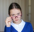 Portrait of beautiful young schoolgirl in school uniform looking over the top of her glasses. Royalty Free Stock Photo