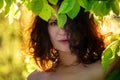 Portrait of a beautiful young sensual brunette woman standing in golden sunlight under a green tree and enjoying nature and forest