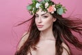 Portrait of beautiful young sexual sensual woman with perfect skin make up streaming hair and flowers on head on pink background. Royalty Free Stock Photo