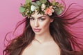 Portrait of beautiful young sexual sensual woman with perfect skin make up streaming hair and flowers on head on pink background. Royalty Free Stock Photo